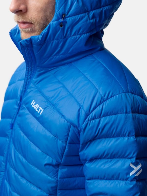 A person wearing a bright blue, quilted Halti jacket with a hood. The logo HALTI is visible on the chest and another logo is on the sleeve. The background is plain and light-colored.