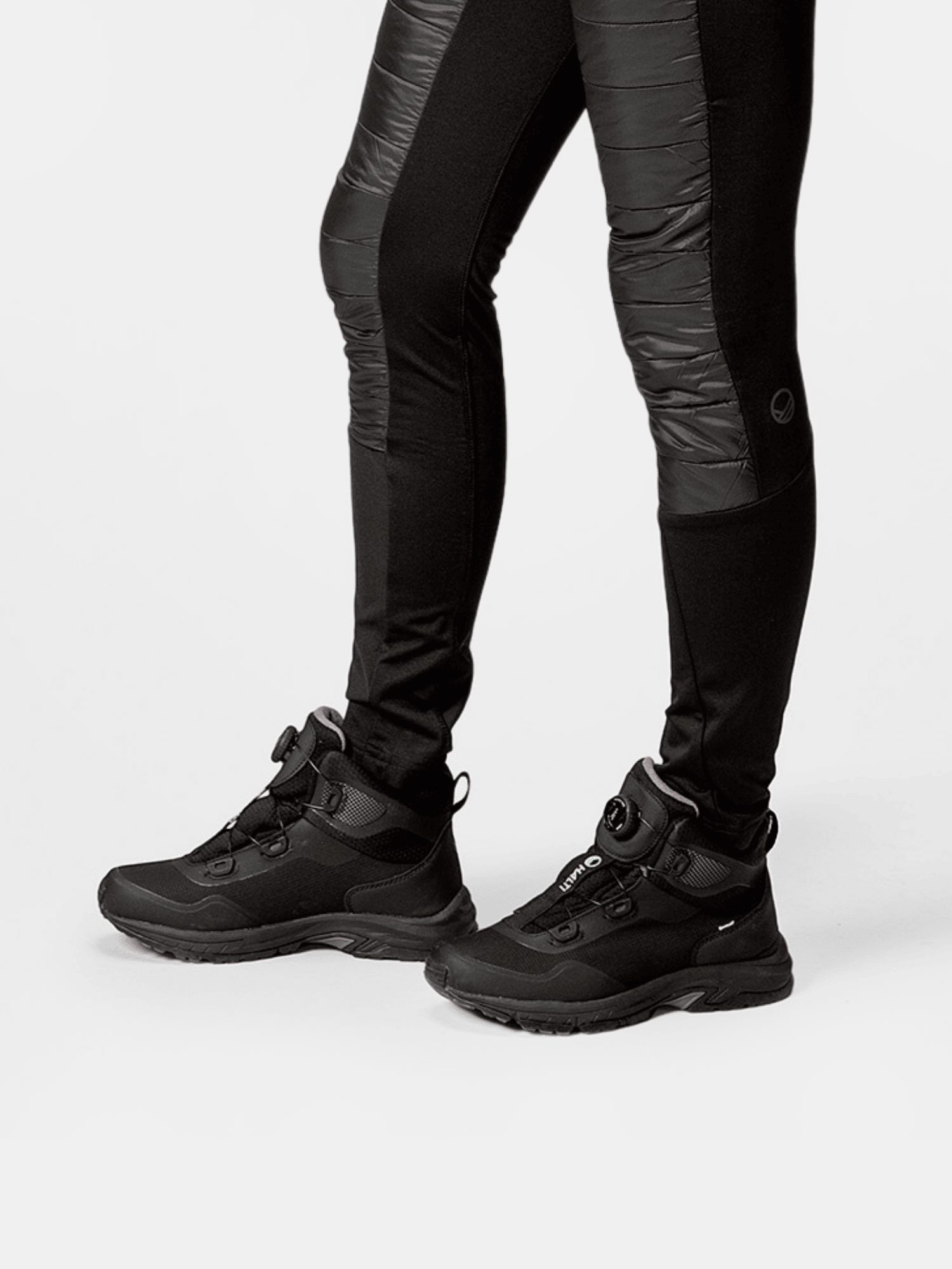 Person wears black athletic pants and Halti Fara Mid DrymaxX Freelock outdoor shoes, standing on a white background.