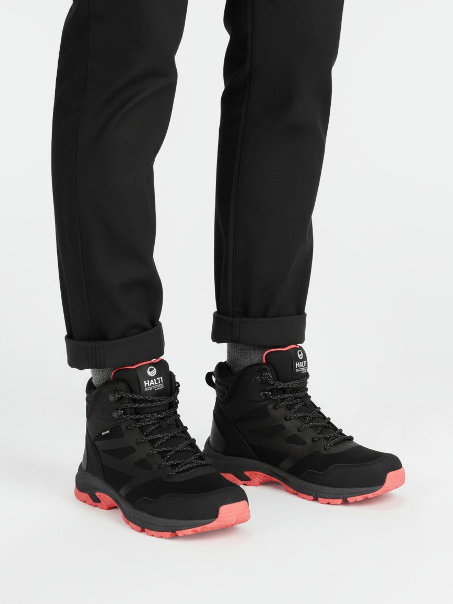 A person in black pants wears Halti Polaris Women's Mid 2 DrymaxX Outdoor Shoes with pink soles on a white background.