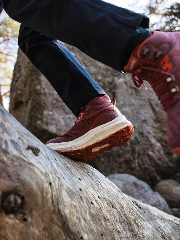 A woman in Halti Rapid DX Mid Outdoor Shoes and black pants steps onto a large rock outdoors.