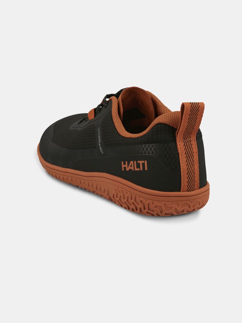 The Halti Tuntuma Barefoot Shoe is a black and orange zero-drop sneaker with a textured sole for natural walking.