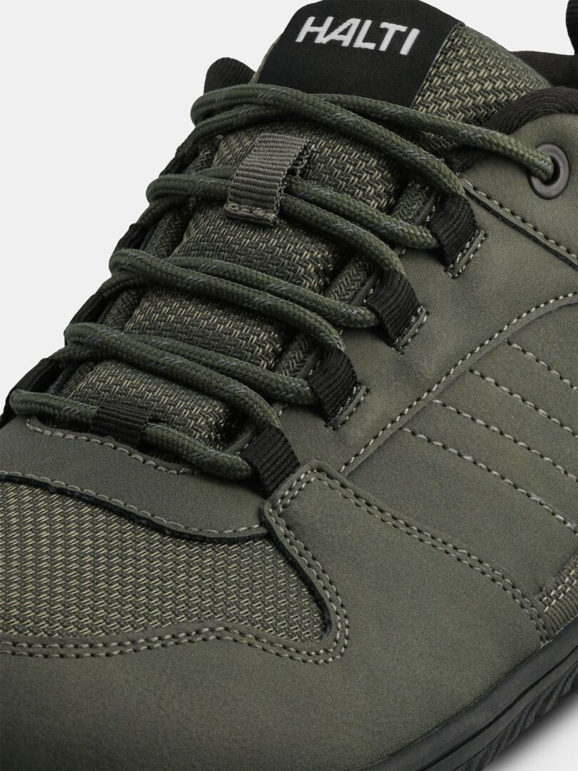 A close-up of a green Tuntuma DX Barefoot Shoe Men's with black laces and Halti branding on the tongue.