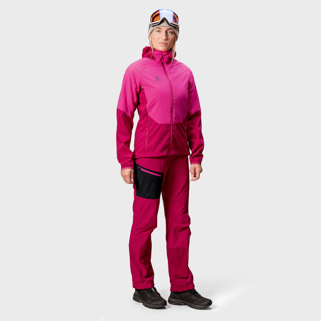 A person faces forward in a bright pink Halti Crust Womens Layer Jacket, pants, black shoes, and ski goggles.