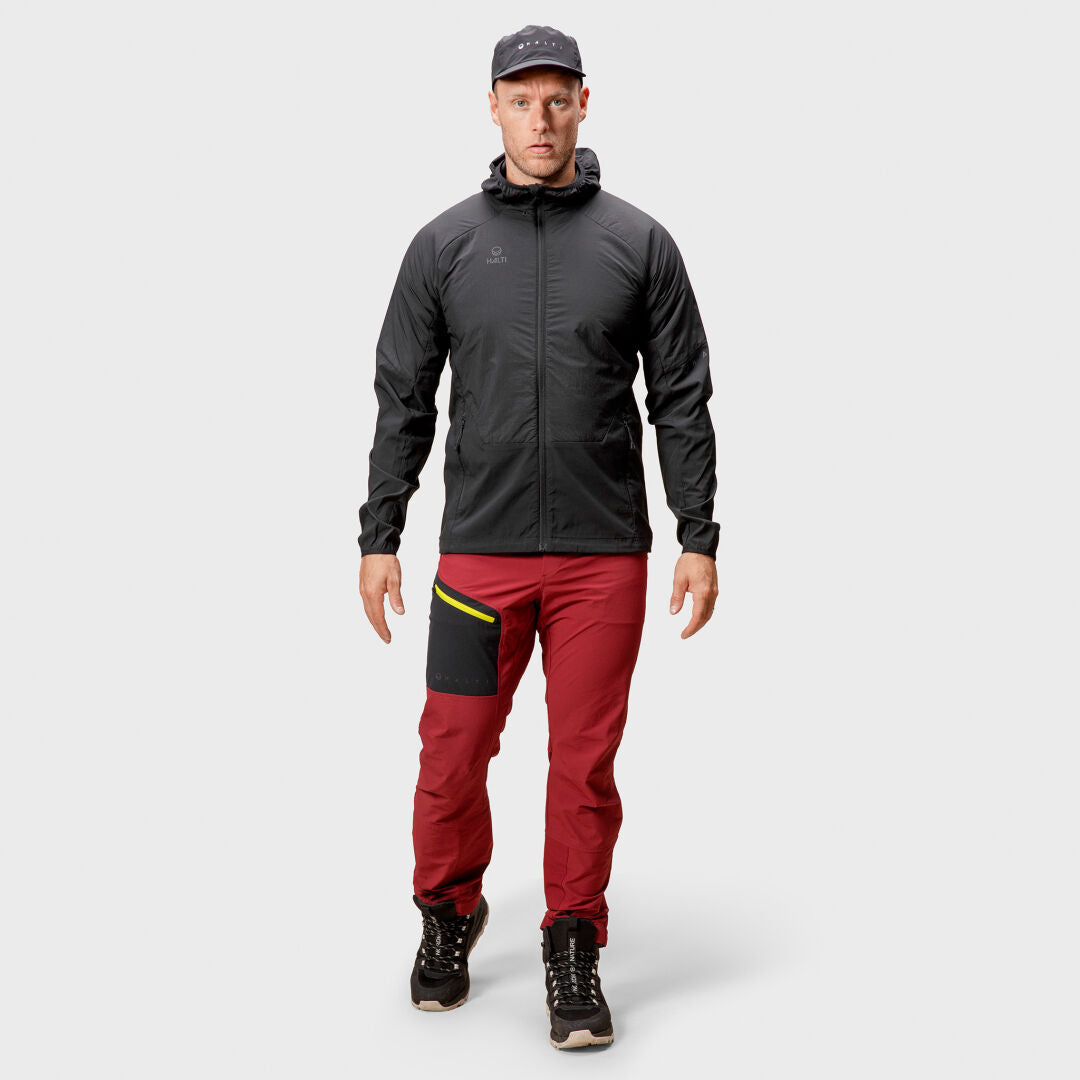 Man wearing Halti Crust Mens Layer Jacket, red pants with black pocket, black cap and boots, on white background.
