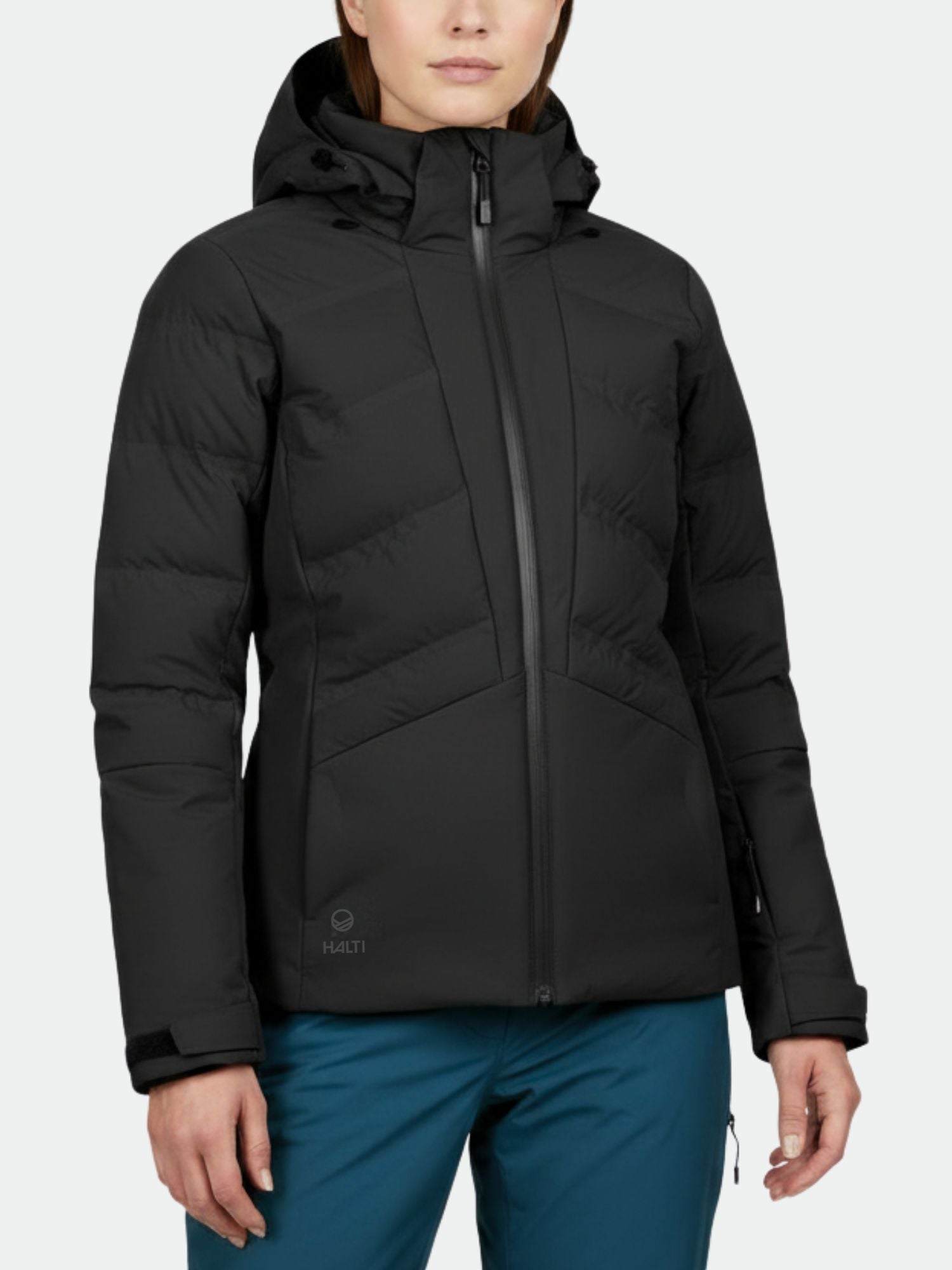 A woman in a Halti Nordic Arcty Ski Jacket and blue pants stands against a plain light background.