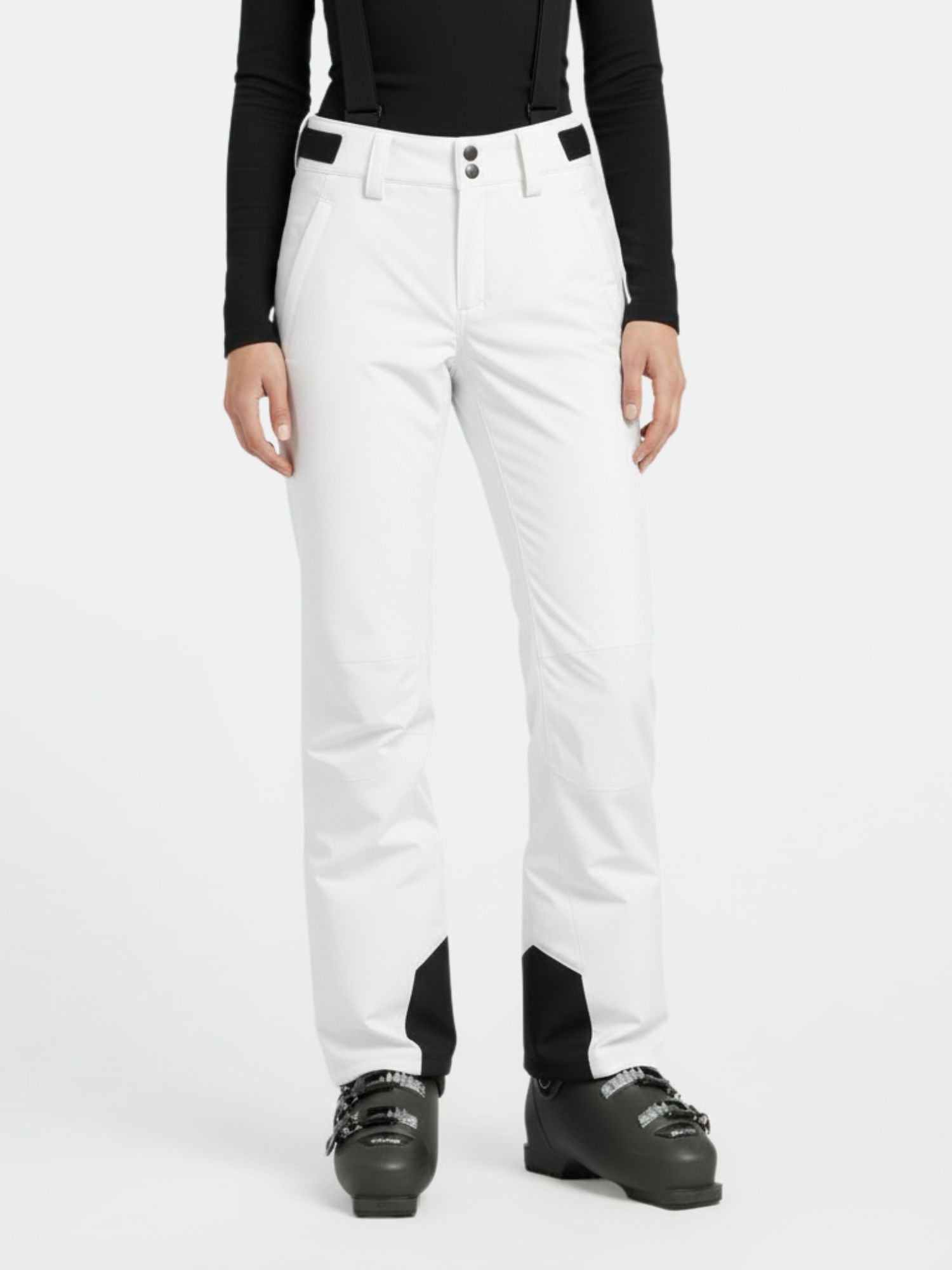 A woman wears Halti Trusty DrymaxX Ski Pants in white with black suspenders, a black top, and ski boots.