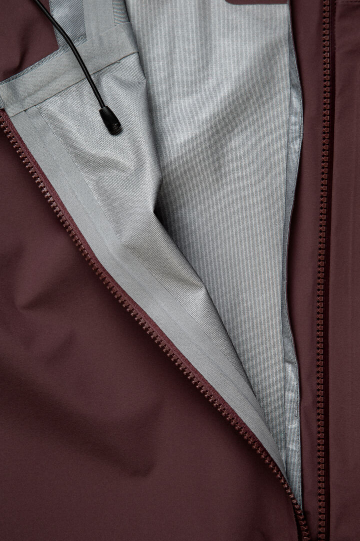 Close-up of a maroon Halti Settler 3L DX Ski Jacket Men’s open zipper, showing gray lining and black cord lock.