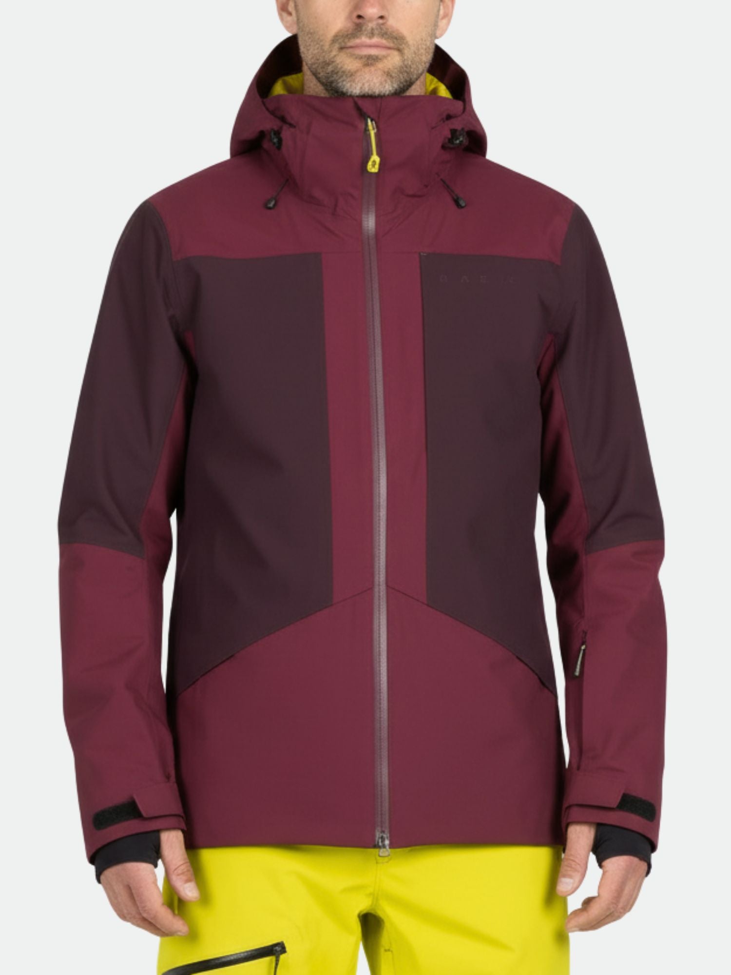 A man wears the Halti Planker DrymaxX maroon ski jacket with yellow zippers and bright yellow pants, facing forward.