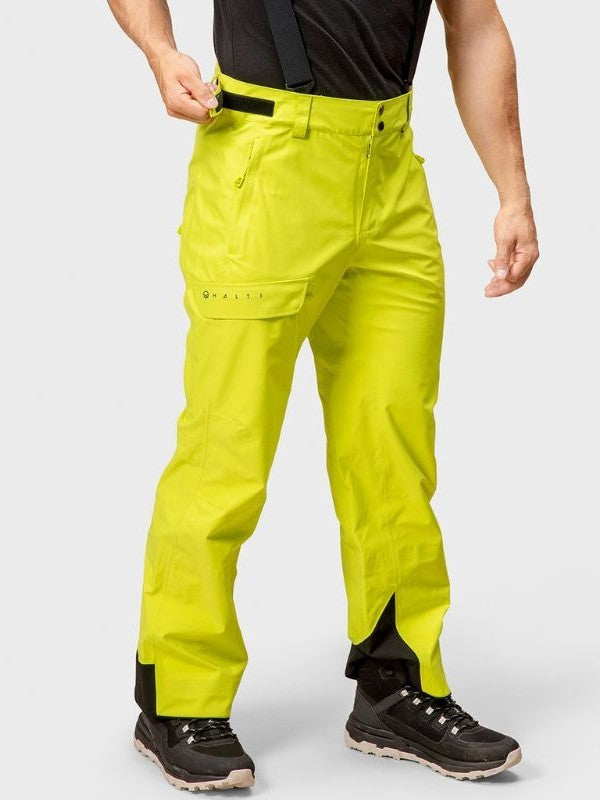 A man wears Halti Settler 3L DrymaxX Ski Pants in bright yellow with black suspenders and shoes, against a plain background.