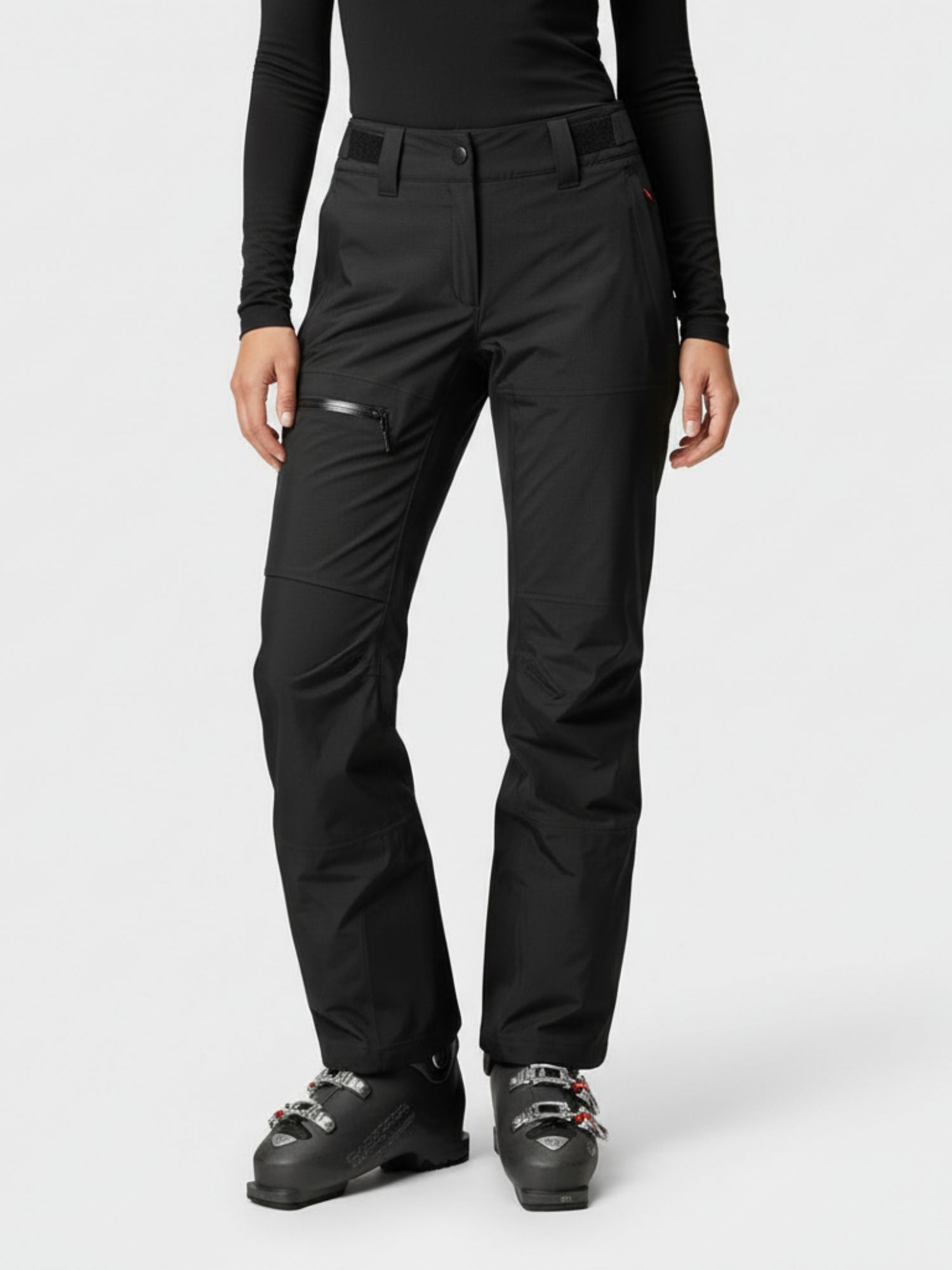 A person wears Halti Alpine 3L DrymaxX Shell Pants Women's, a black long-sleeve top, and black ski boots against a plain background.
