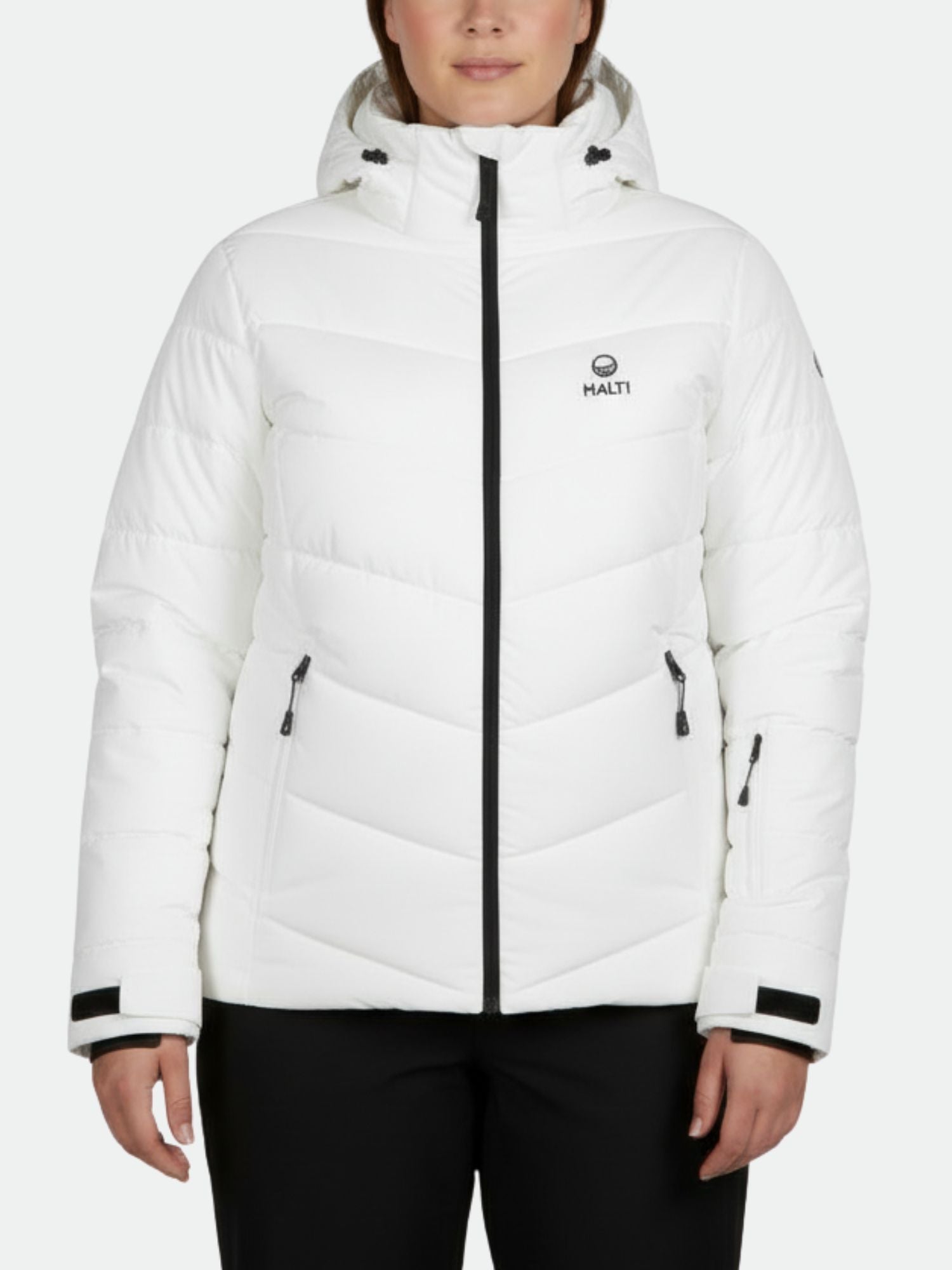 A person wears a Halti Mellow Plus Puffer Ski Jacket for women in white with black zippers and logo, paired with black pants.