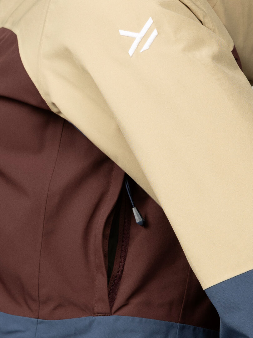 Close-up of Halti Gracer DX Ski Jacket Women's: beige sleeve with white logo and brown zippered pocket.