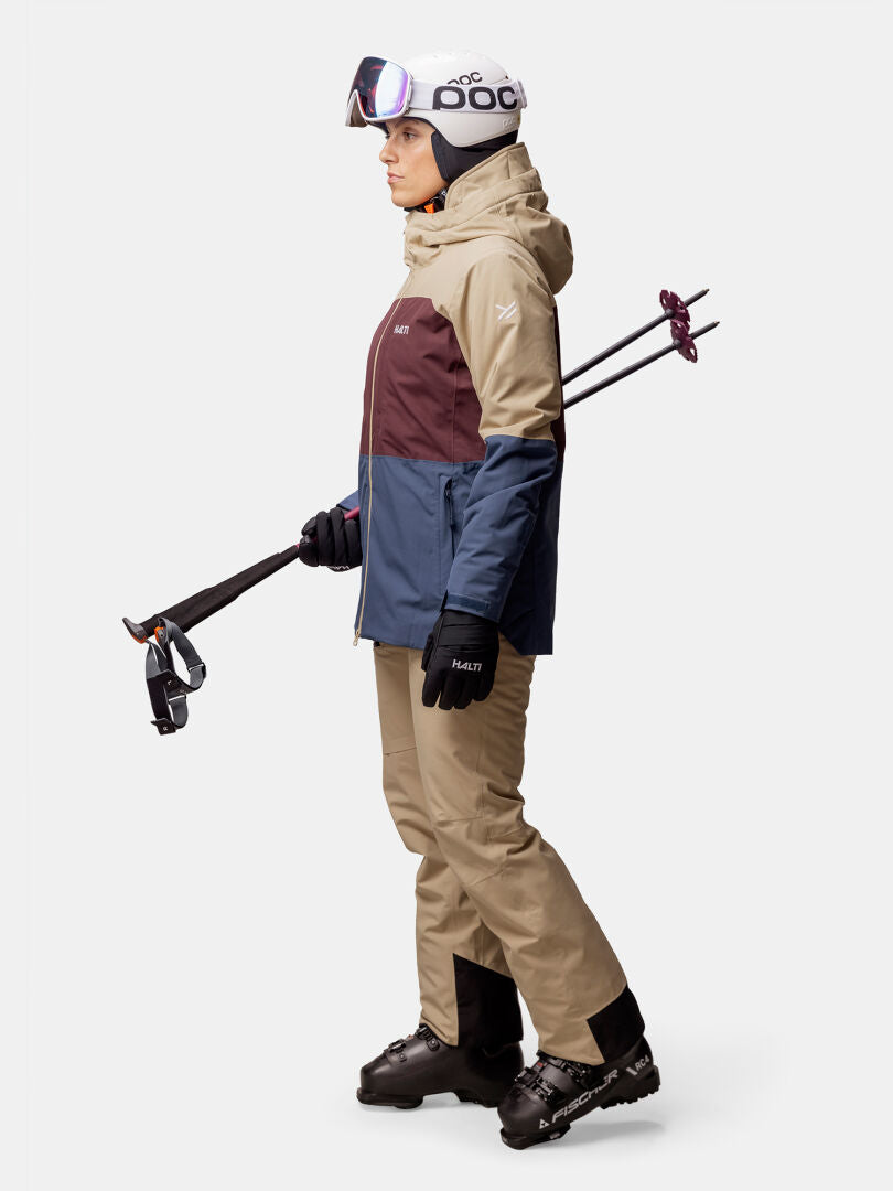 Woman wearing the Halti Gracer DX Ski Jacket holds ski poles and gloves, ready for skiing against a plain background.