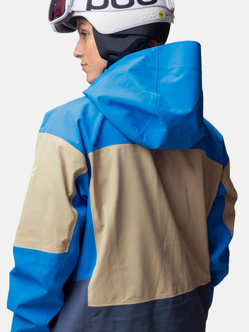 Person wears a Halti Rizle 3L DX Ski Jacket (blue/beige), white helmet, and goggles; shown from back and side.
