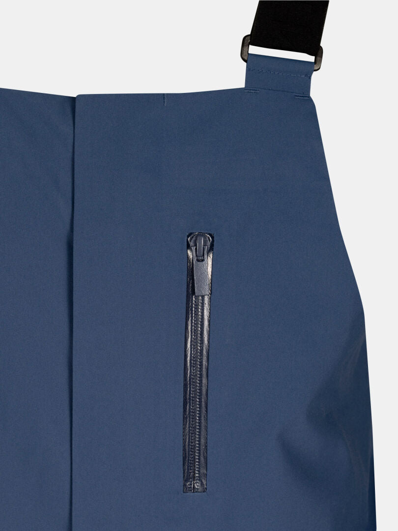 Close-up of blue Rizle 3L Dx Ski Pants Unisex with a zippered chest pocket and black suspender strap.