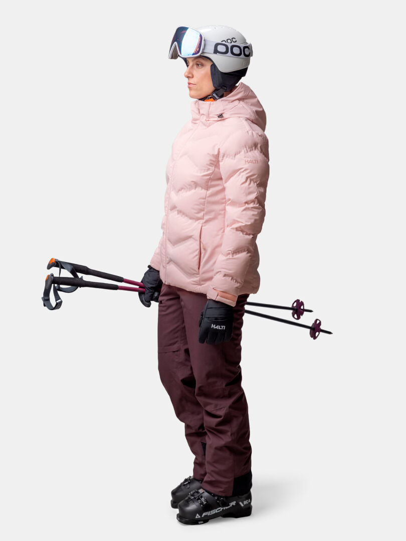 Person in ski gear holds ski poles, wearing Halti Nordic Arcty II Women's Ski Jacket, maroon pants, gloves, helmet, goggles.