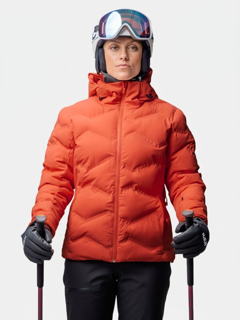 Woman wears the Halti Nordic Arcty II Ski Jacket, ski helmet, and goggles while holding poles against a plain background.