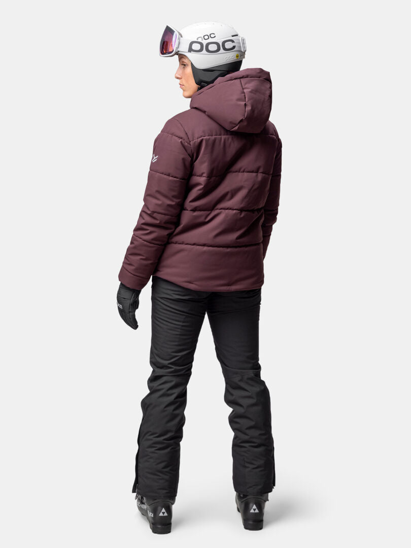 A person wears the Halti Ascale Puffer Ski Jacket for women, black pants, gloves, and a white ski helmet facing away.