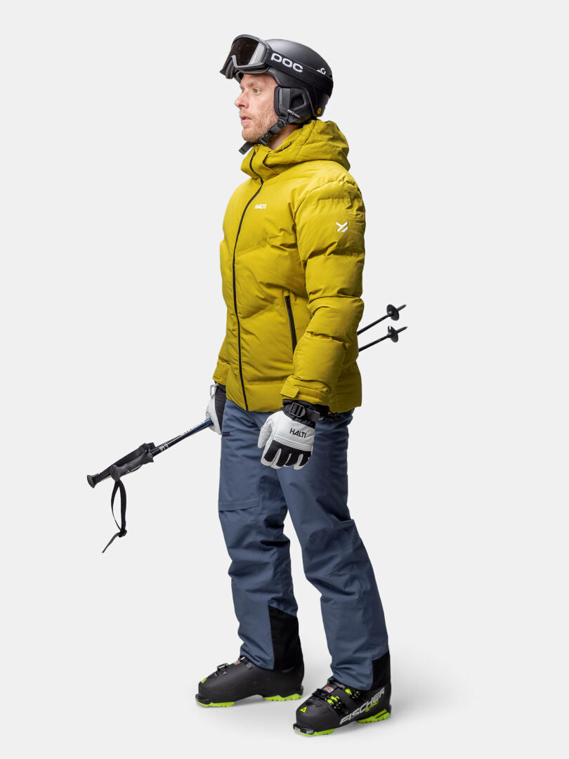 A man in a Halti Nordic Arcty II Ski Jacket, blue pants, and gear stands facing left.
