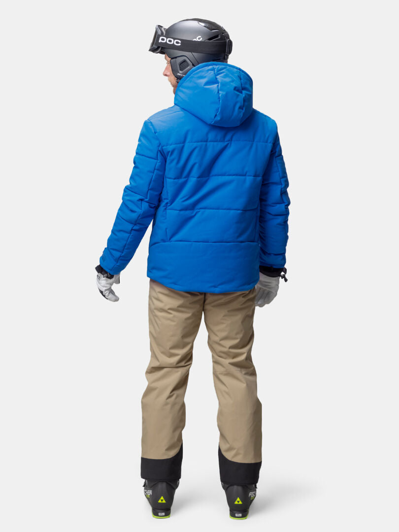 Person in a Halti Ascale Puffer Ski Jacket, beige pants, helmet, and ski boots stands with back to camera.