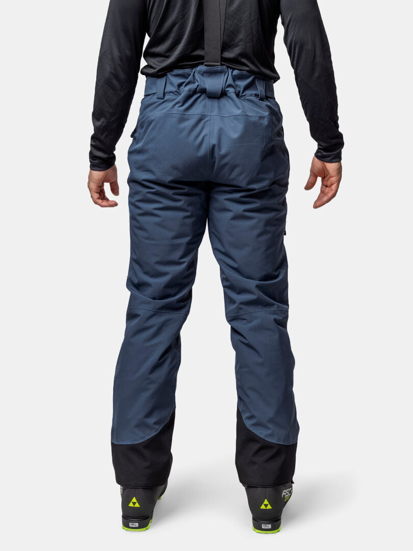 Man in Halti Carvey II DX blue ski pants with black suspenders and boots, seen from the back on plain background.