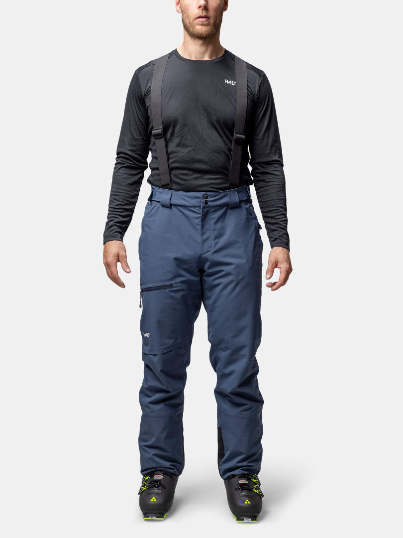 Wearing Halti Carvey II DX men's blue insulated ski pants with suspenders, a black long-sleeve shirt, and black ski boots.