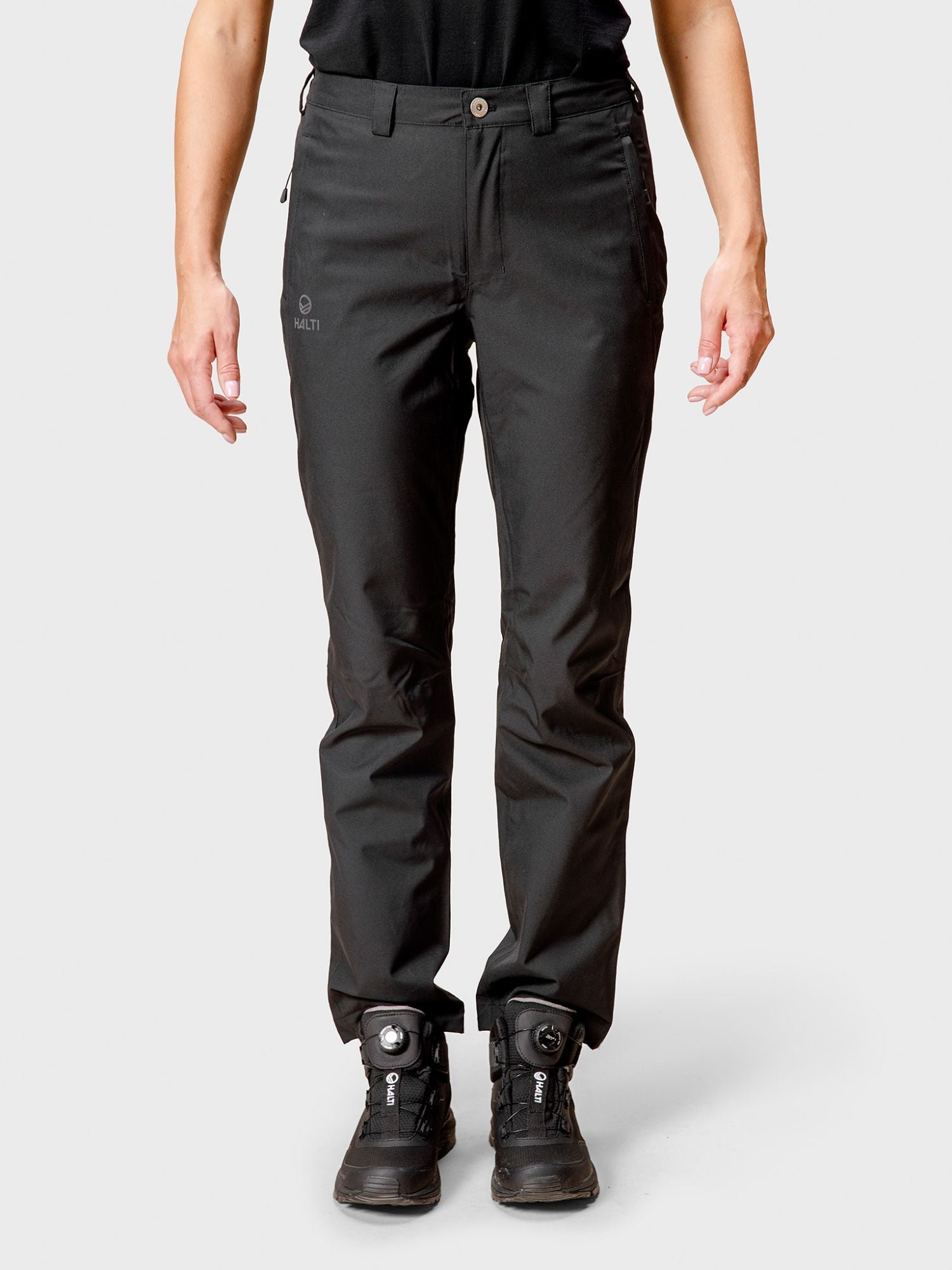 A person wears Halti Leisti DX Shell Pants Women's in black with black boots, shown from shoulders to feet.