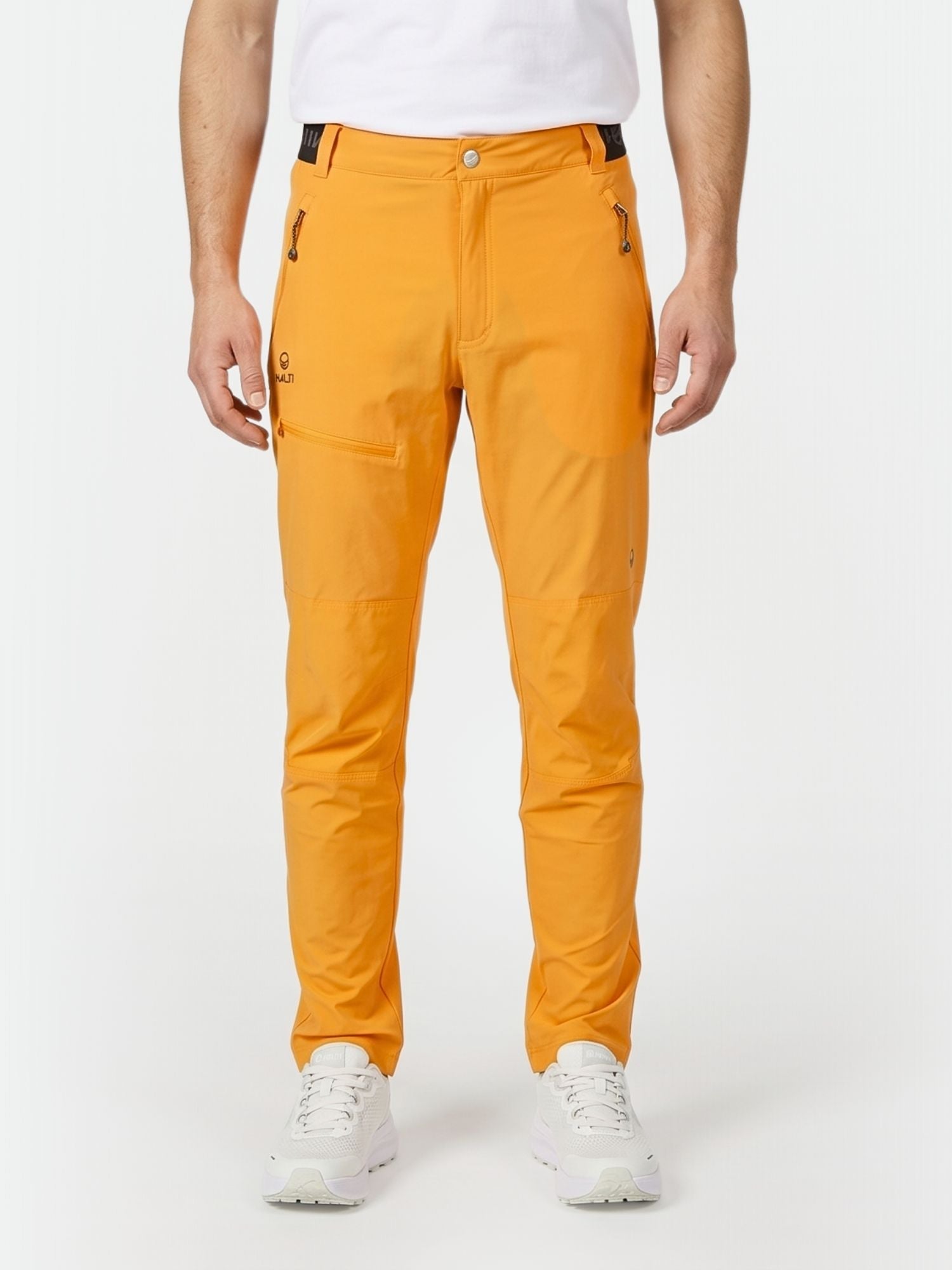 A person in Halti Pallas Men's X-stretch Lite Pants (bright orange), white shirt, and sneakers stands against a white background.