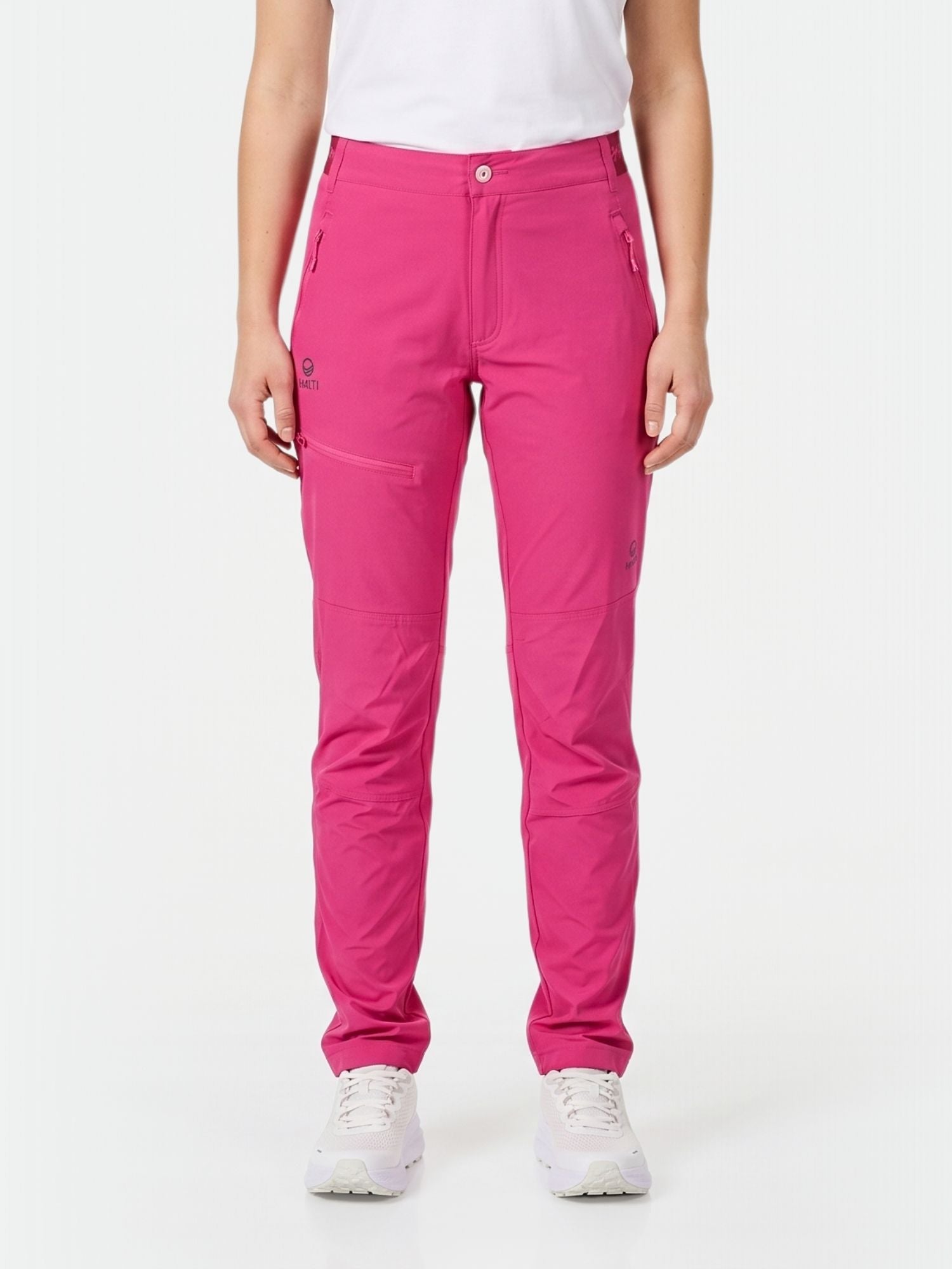A woman wears Halti Pallas Women's X-stretch Lite Pants in bright pink with a white tee and sneakers against a white background.