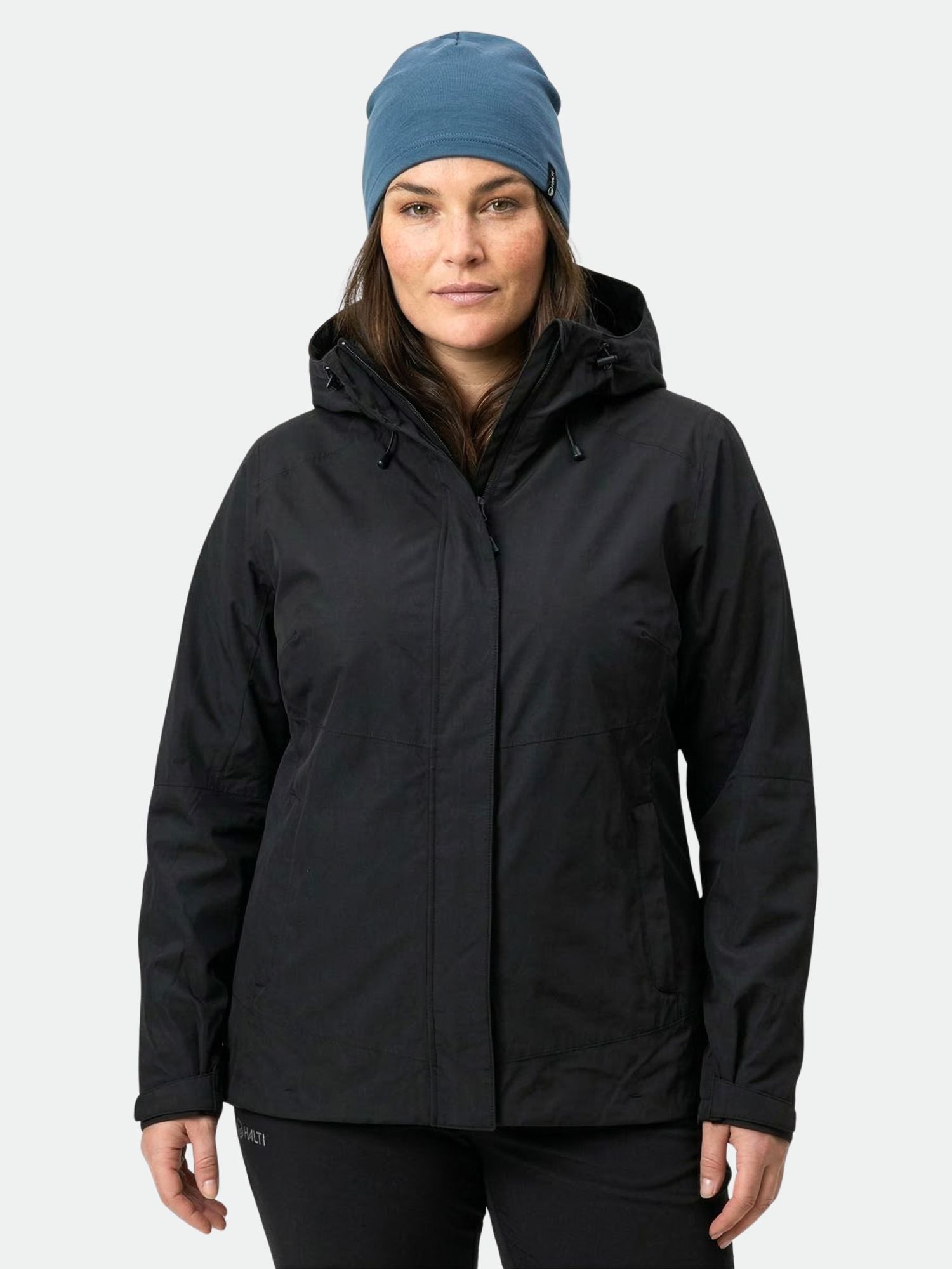 A woman wears the Halti Fort Plus Women's DrymaxX Shell Jacket and a blue beanie, facing the camera.