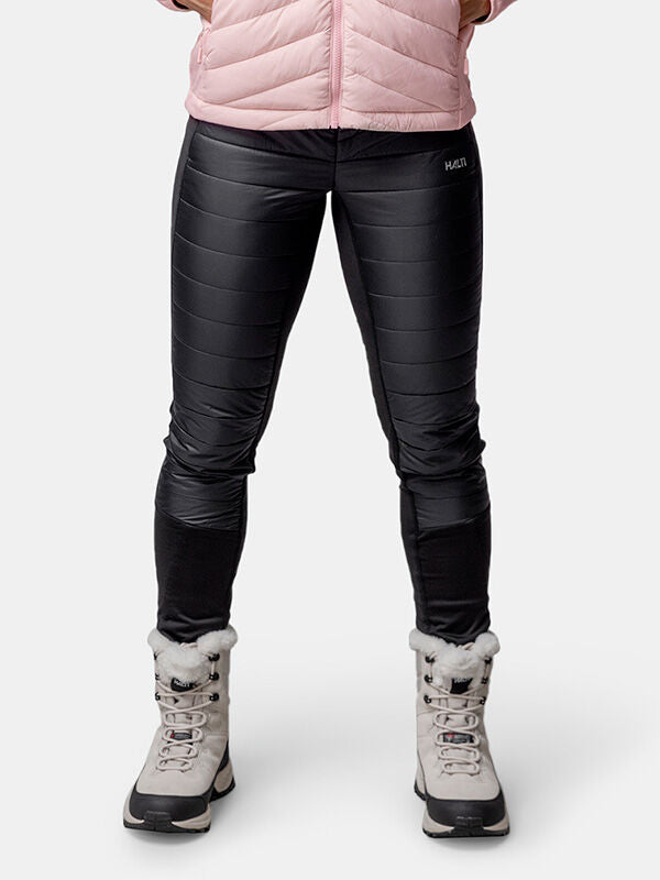 A person in a pink jacket, Halti Veidnes Insulation Pants Womens, and gray fur-trimmed boots stands against a white background.