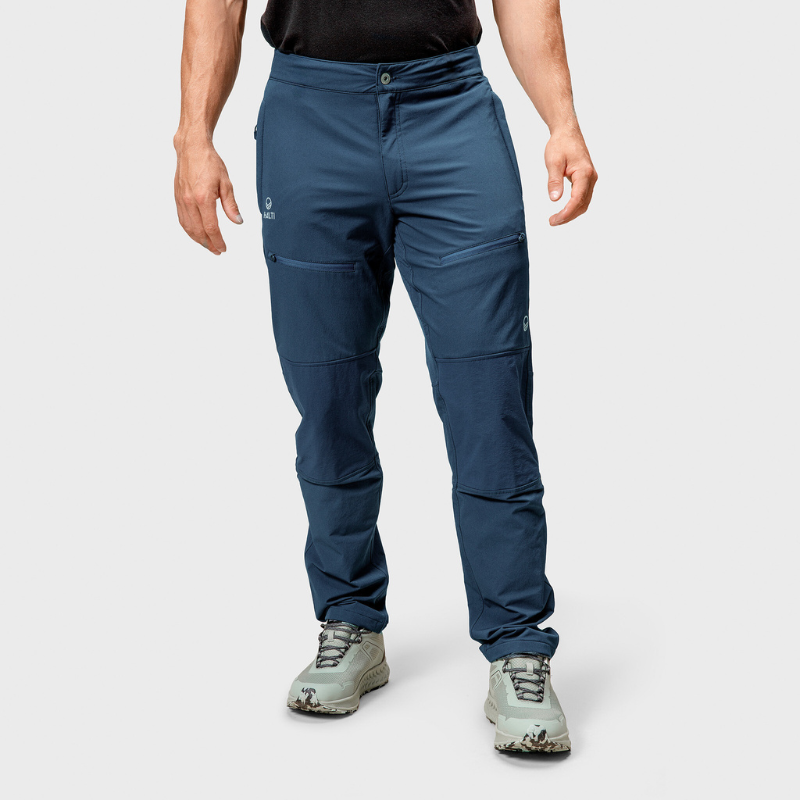 A person wears Halti Pallas II Mens Warm X-stretch blue pants and gray hiking shoes against a plain light background.