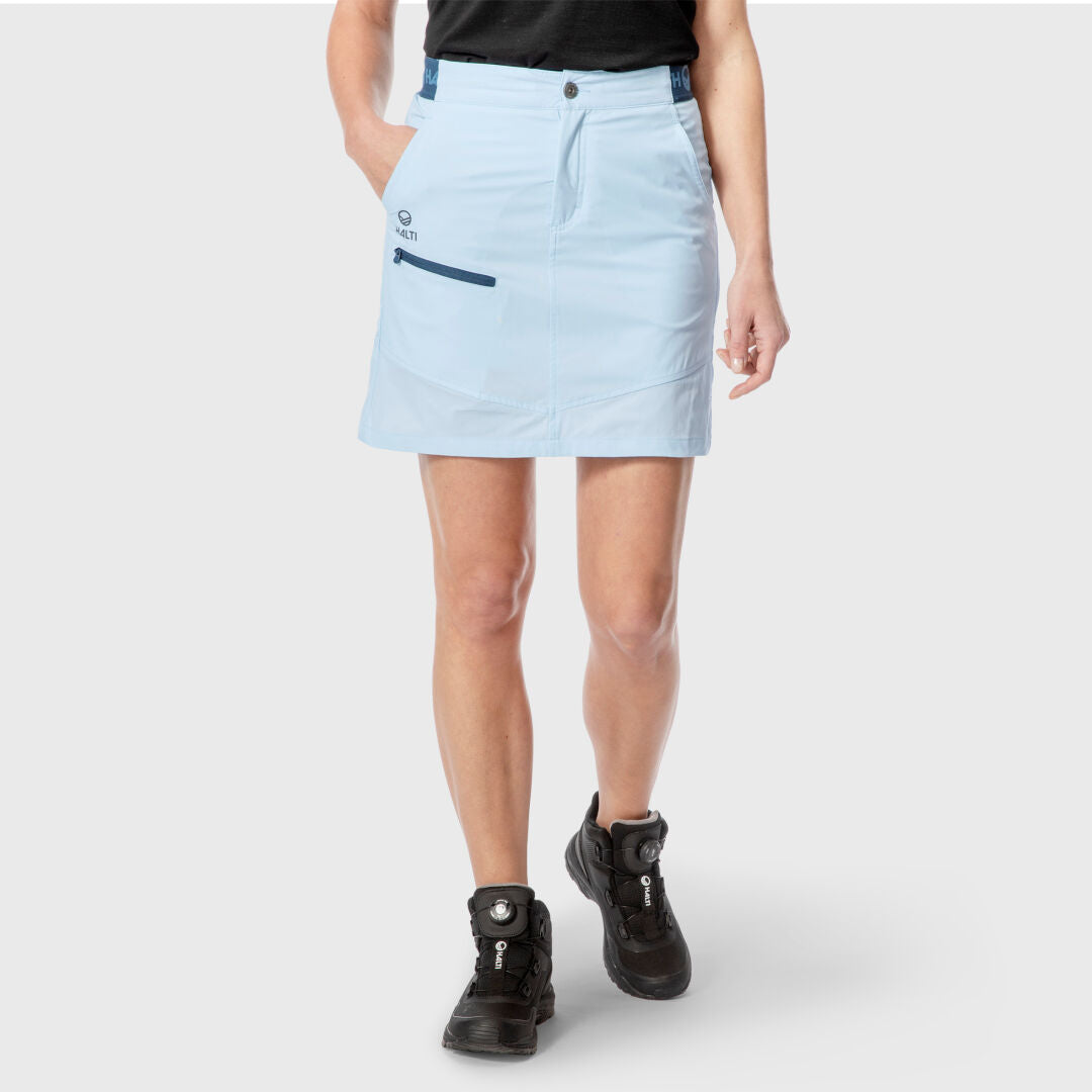 Person wearing a Halti Pallas Lite X-stretch Skort Women's in light blue, black t-shirt, and black boots on a plain background.