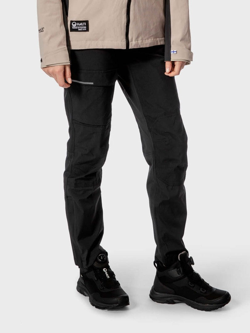 Person wearing Halti Hiker Women's DrymaxX Pants in black, black boots, and a beige jacket against a plain background.