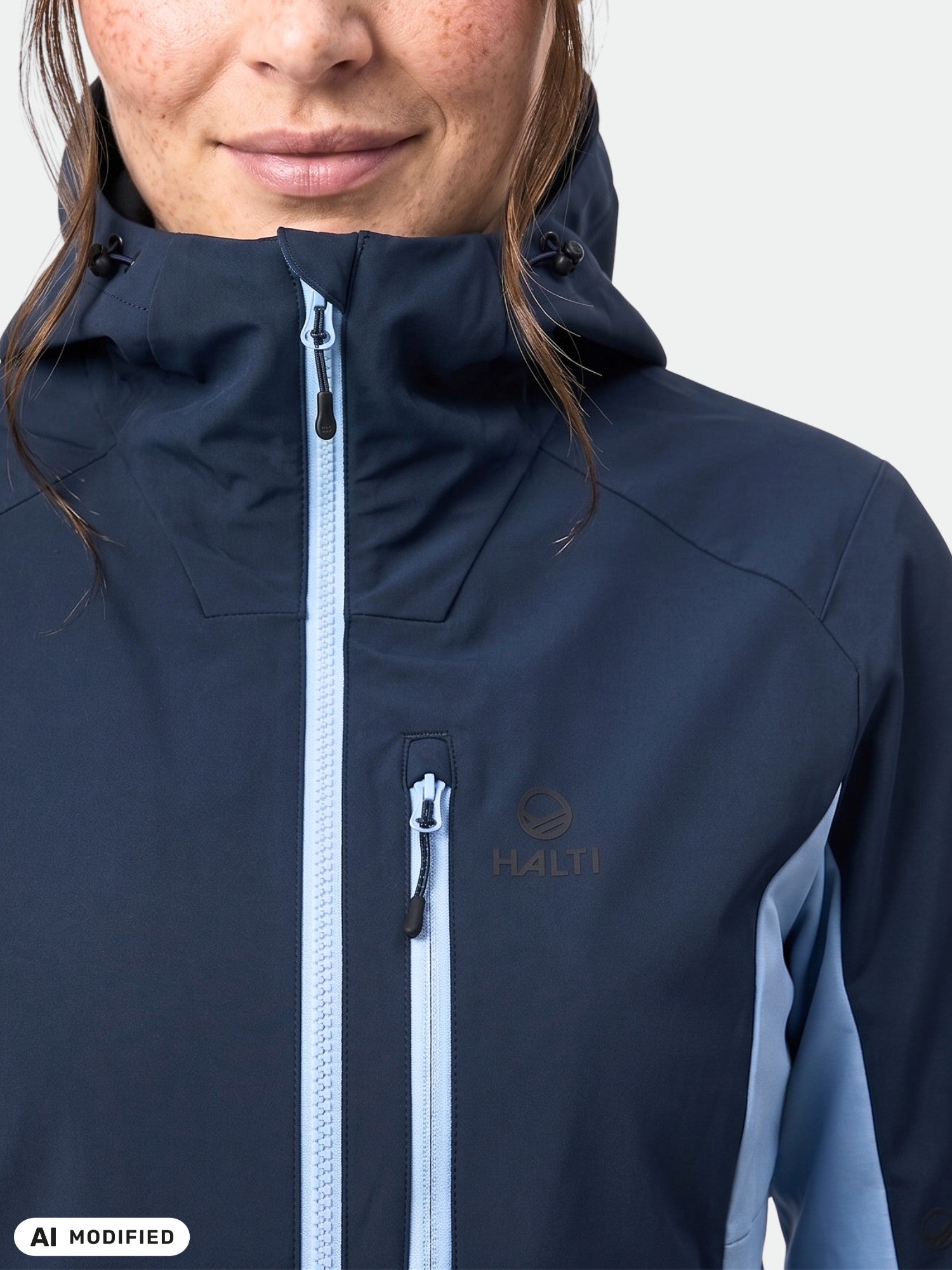 Woman wears Halti Pallas Plus III navy hybrid jacket with high collar and light blue zippers, shown from shoulders up.