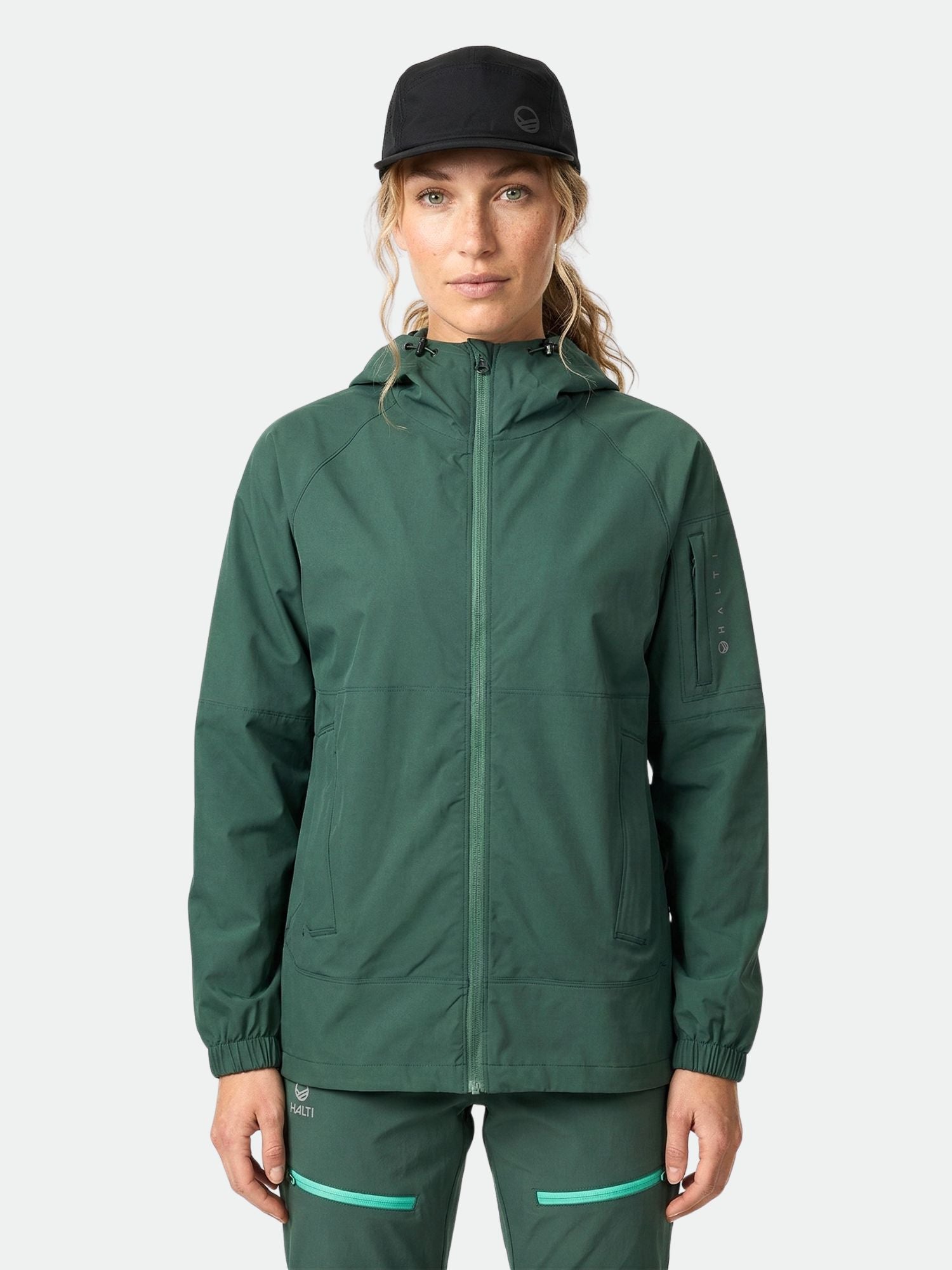 A woman wears the Halti Pallas Women's Jogger Lite Jacket, matching pants, and a black cap against a plain background.