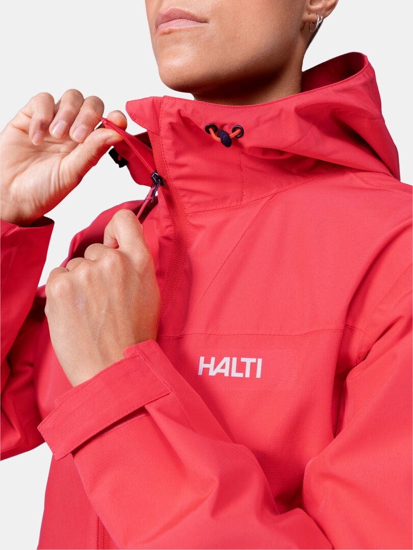 Woman zipping up a red Halti Forter DX Shell Jacket, shown from the shoulders up against a plain background.