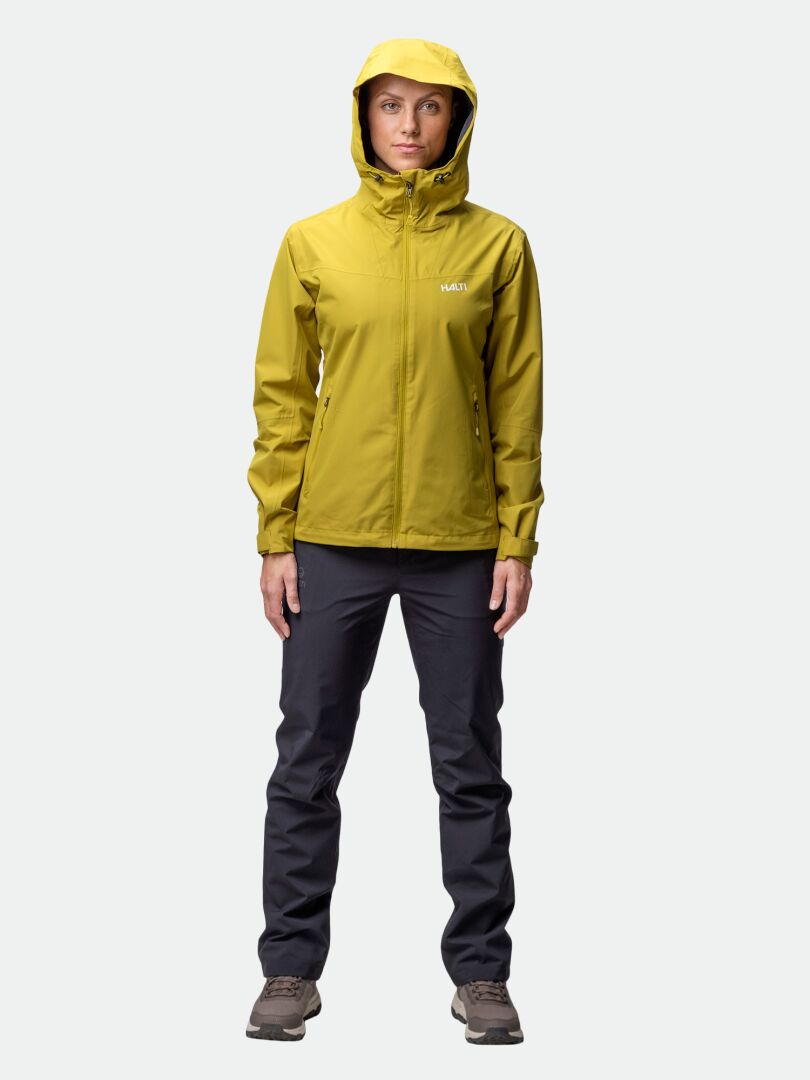 A person faces forward wearing a yellow Halti Forter DX Shell Jacket, dark pants, and brown shoes against a plain background.