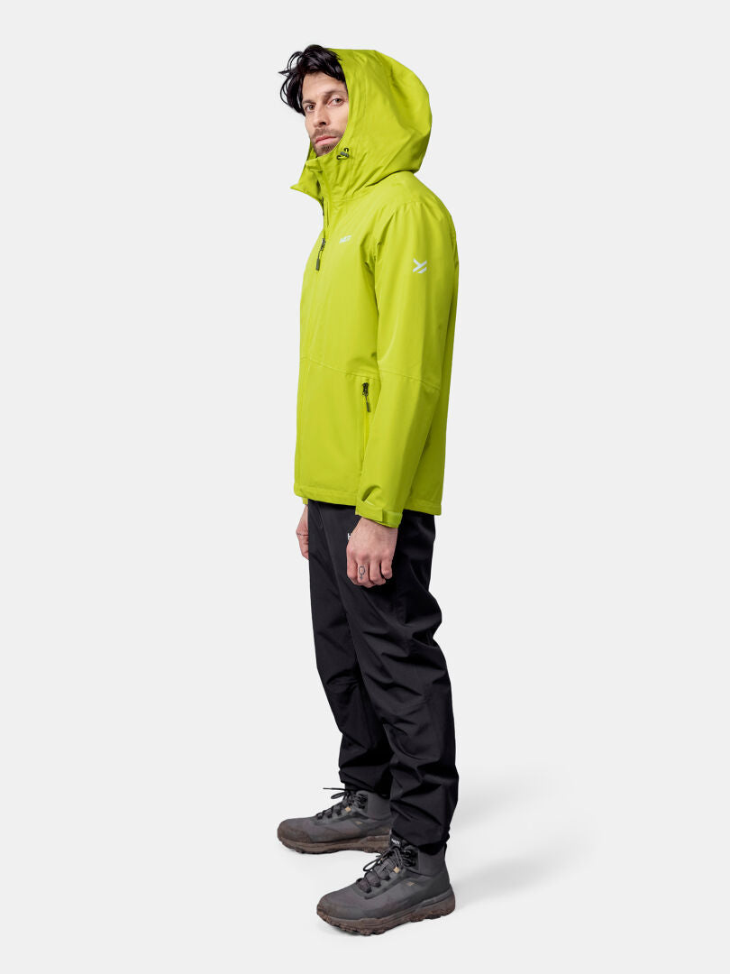 A man in profile wears a lime green Halti Forter DX Shell Jacket, black pants, and gray hiking boots against a plain background.