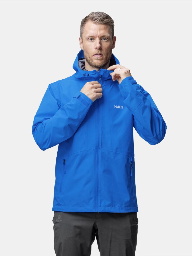A man in a bright blue Halti Forter DX Shell Jacket zips up the waterproof jacket while facing forward.
