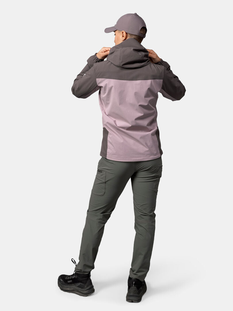 Person faces away wearing Halti Pallas Evo X-stretch Jacket Women’s, green pants, black shoes, and a cap on plain background.