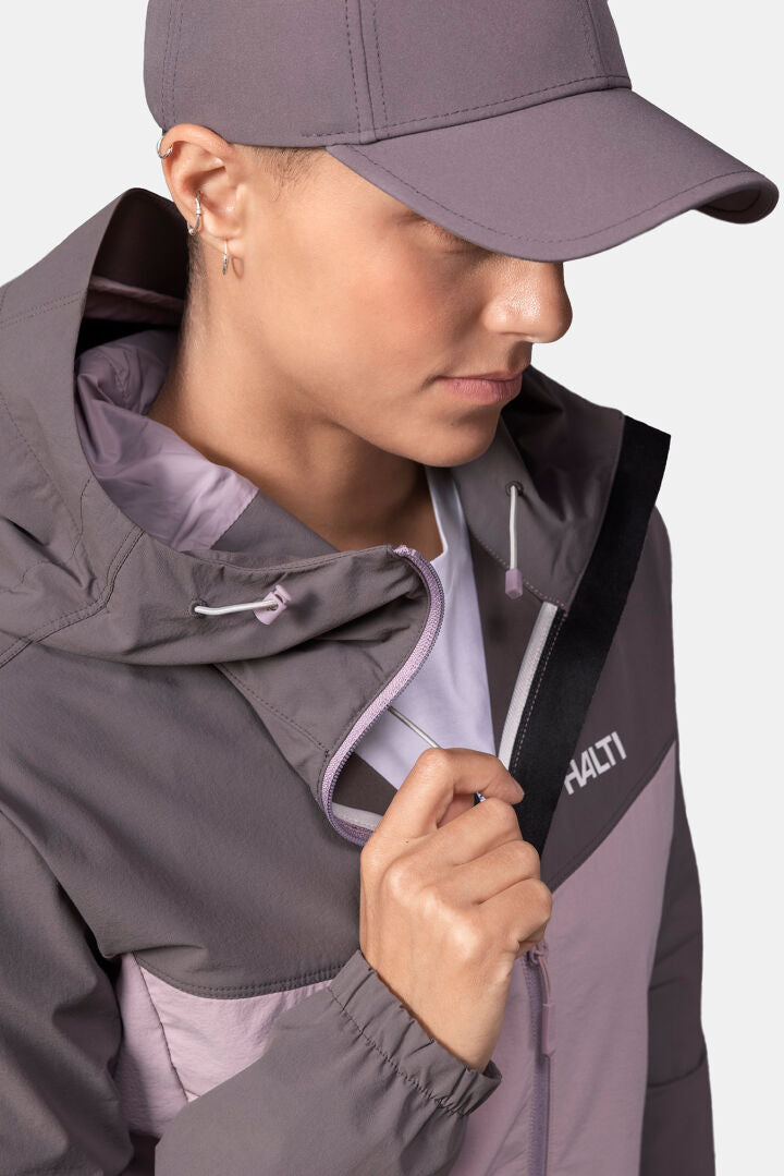 Woman in Halti Pallas Evo X-stretch mauve jacket with zipper, holding collar and looking downward.