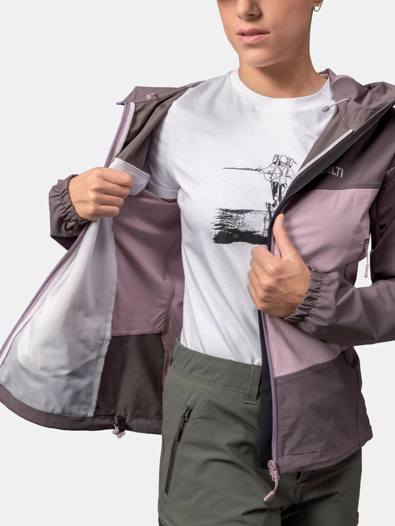 A woman unzips the Halti Pallas Evo X-stretch Jacket, showing a white graphic tee and olive-green pants.