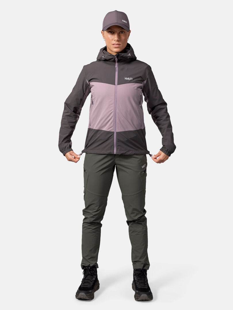 Woman wearing Halti Pallas Evo X-stretch Jacket, cargo pants, black shoes, and a cap standing against a white background.