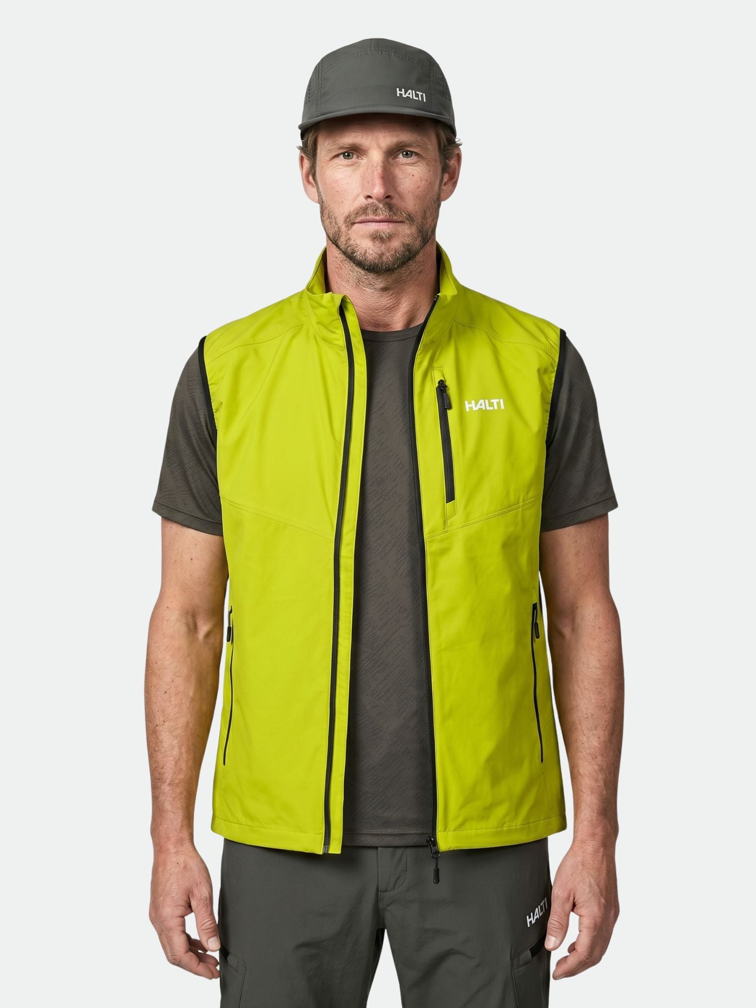 A man wears the Halti Pallas Evo X-stretch Vest over a dark gray T-shirt and cap, standing against a white background.