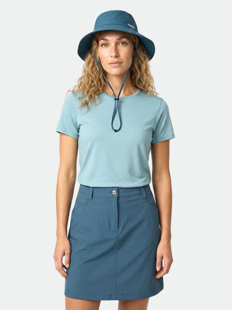 Woman in Halti Pallas Cool Skort, blue bucket hat, and light blue tee against a plain light background.