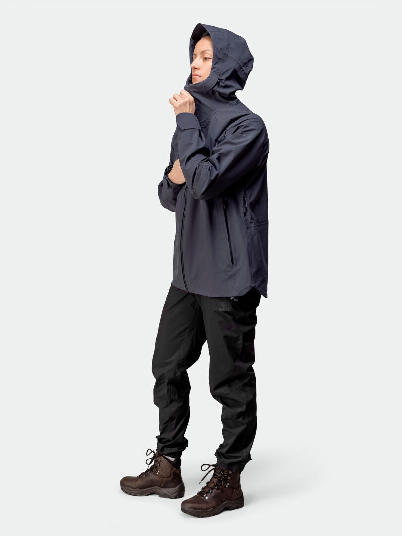 Person in a Halti Kajana 3L DX Shell Jacket, black pants, and brown boots stands against a plain light background.