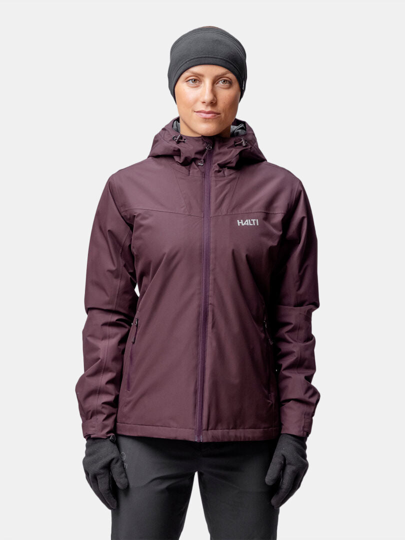 A woman wears the Halti Forter DX Warm Shell Jacket in dark purple, with black gloves and a black beanie, facing the camera.