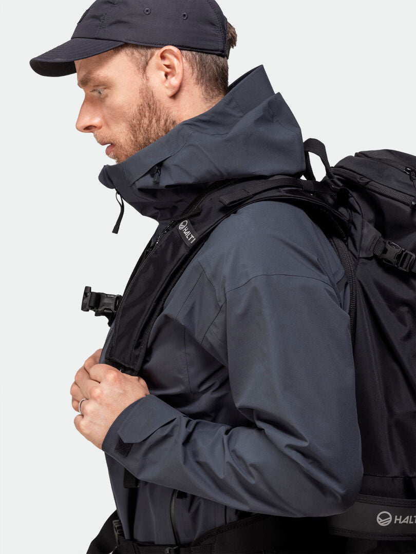 Man wearing the Halti Kajana 3L DX Shell Jacket and cap with backpack, perfect for outdoor enthusiasts, side view.