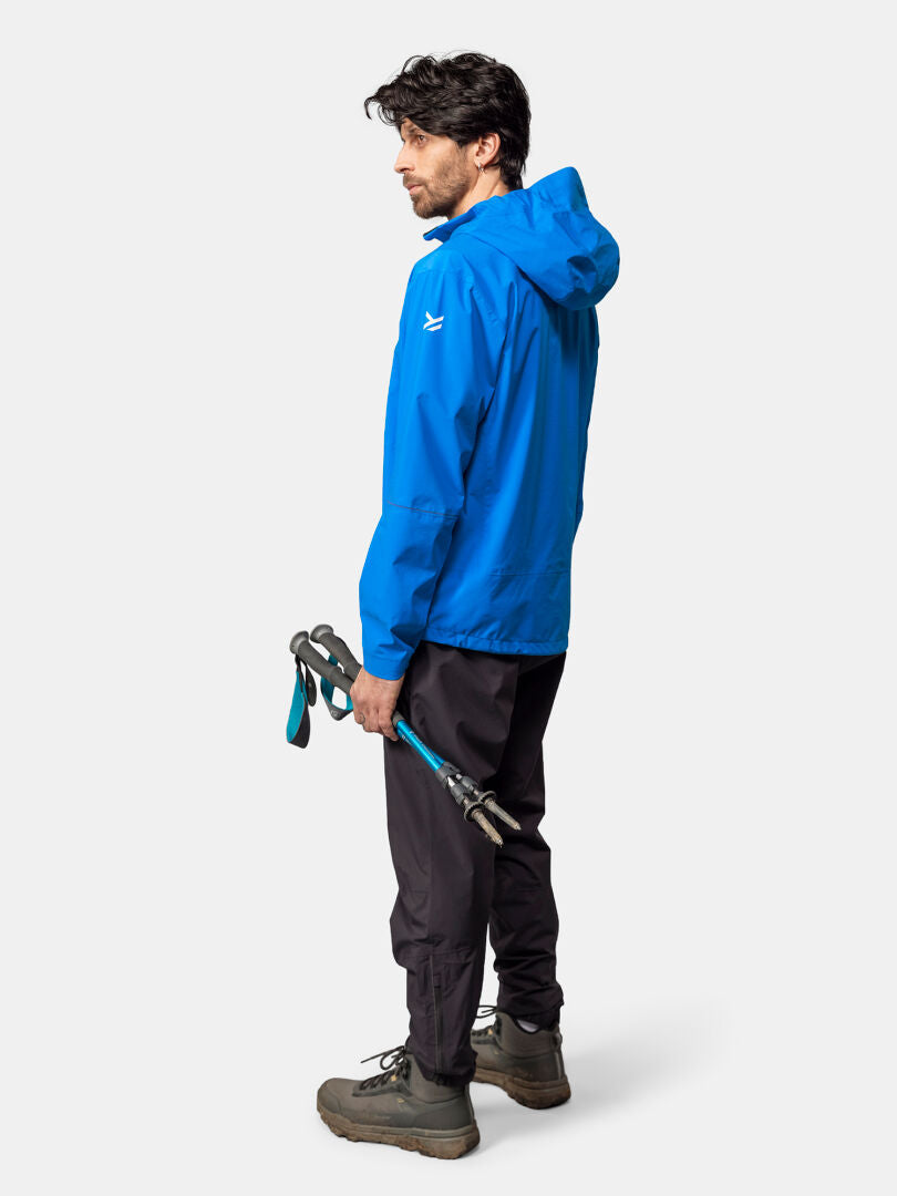A man in a Halti Pisarat 2,5L DX Shell Jacket stands holding trekking poles, facing away at an angle.